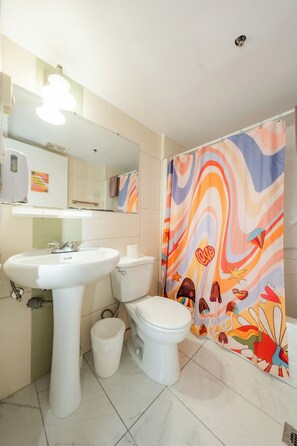 Une salle de bain avec un lavabo blanc, des toilettes et un rideau de douche orné d’un motif abstrait et coloré.