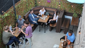 Un espace extérieur aménagé avec des bancs et des tables en bois, entouré d’un mur en treillis recouvert de verdure.