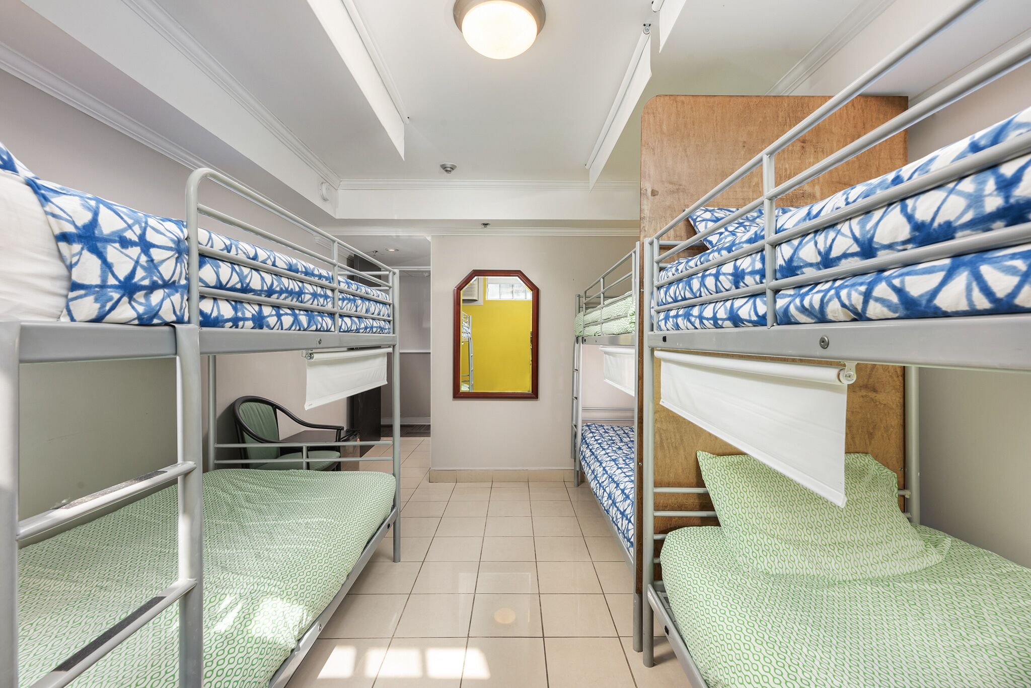 A dormitory room with bunk beds, a mirror, and a window.