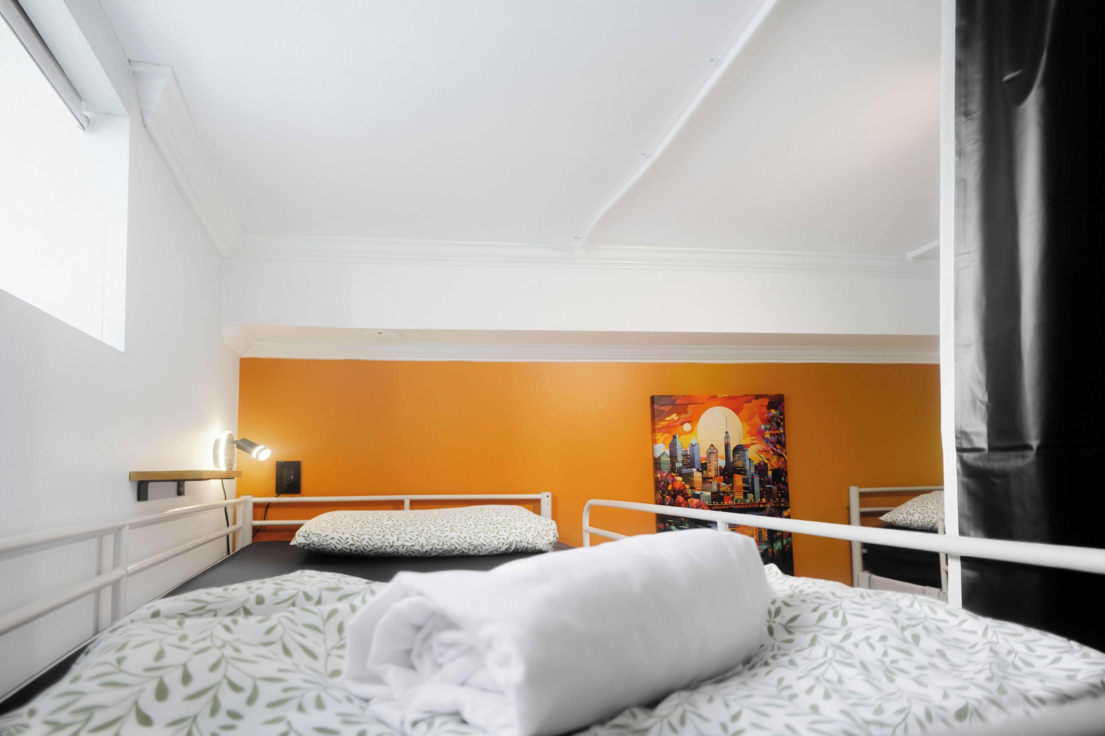 Une pièce avec un lit superposé, un tableau au mur, une fenêtre et un rideau.