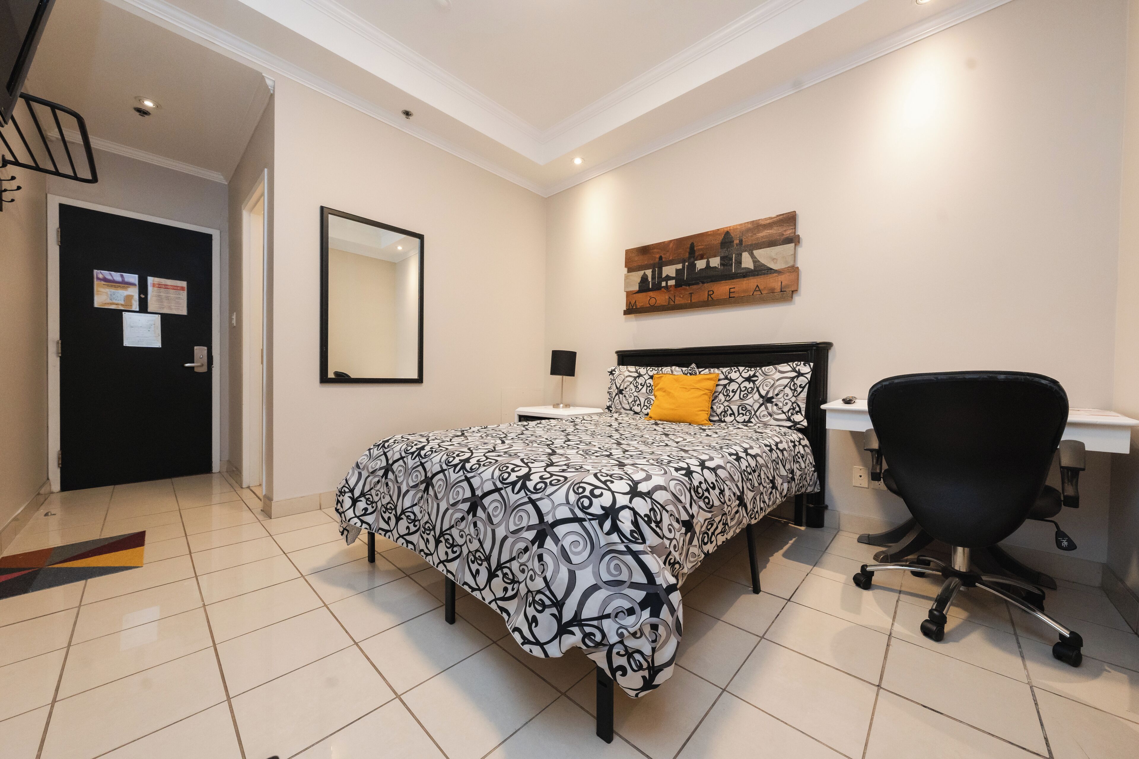 Un dormitorio con cama, escritorio, silla, espejo y un cuadro en la pared.