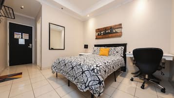 Un dormitorio con cama, escritorio, silla, espejo y un cuadro en la pared.