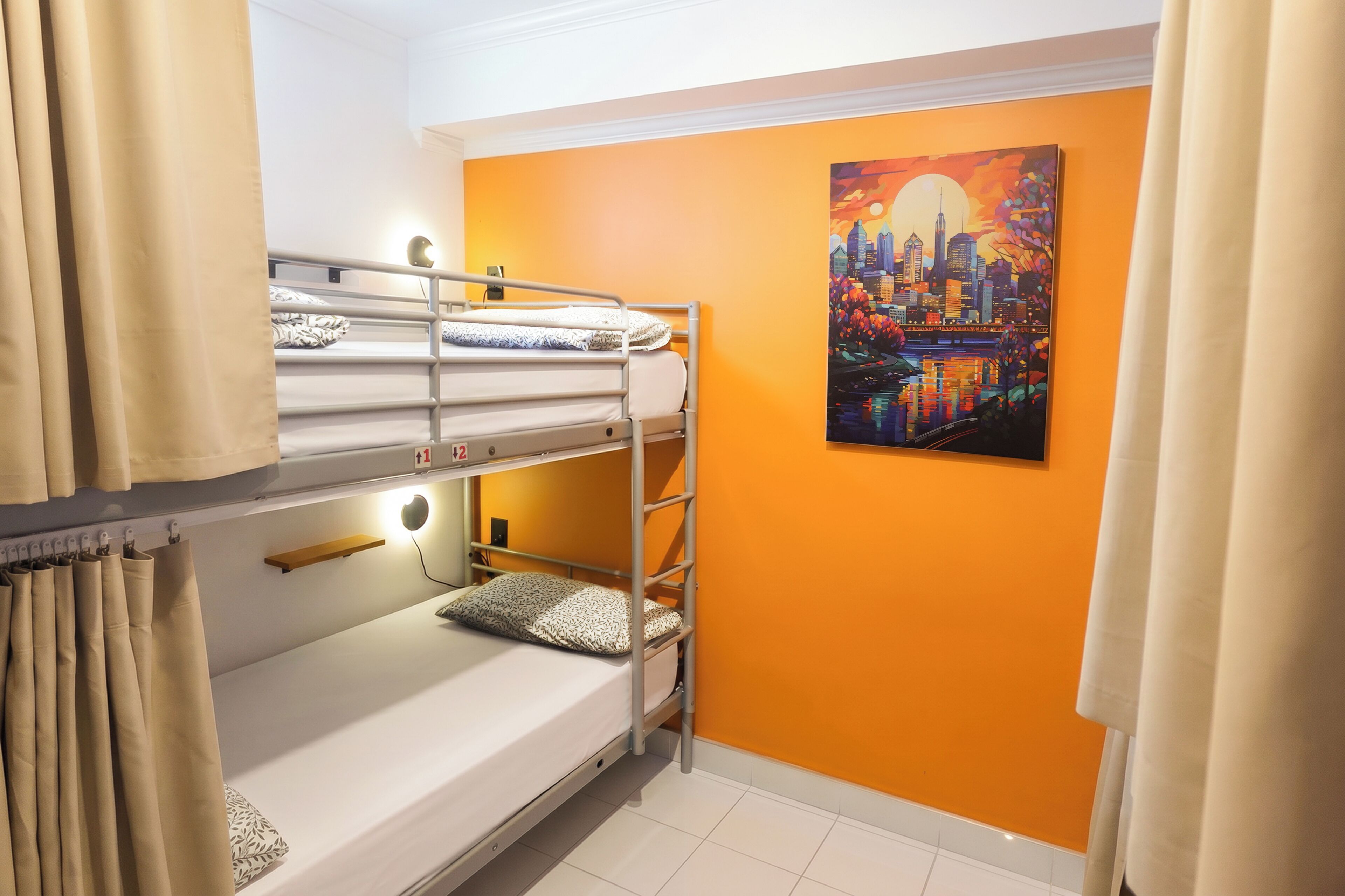 A bunk bed room with a cityscape painting on the wall, a bedside table, and a curtain.