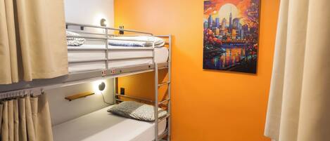 A bunk bed room with a cityscape painting on the wall, a bedside table, and a curtain.