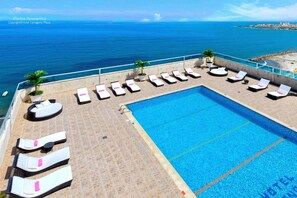 Piscina infinita en la azotea con sillones de descanso y vista al mar.