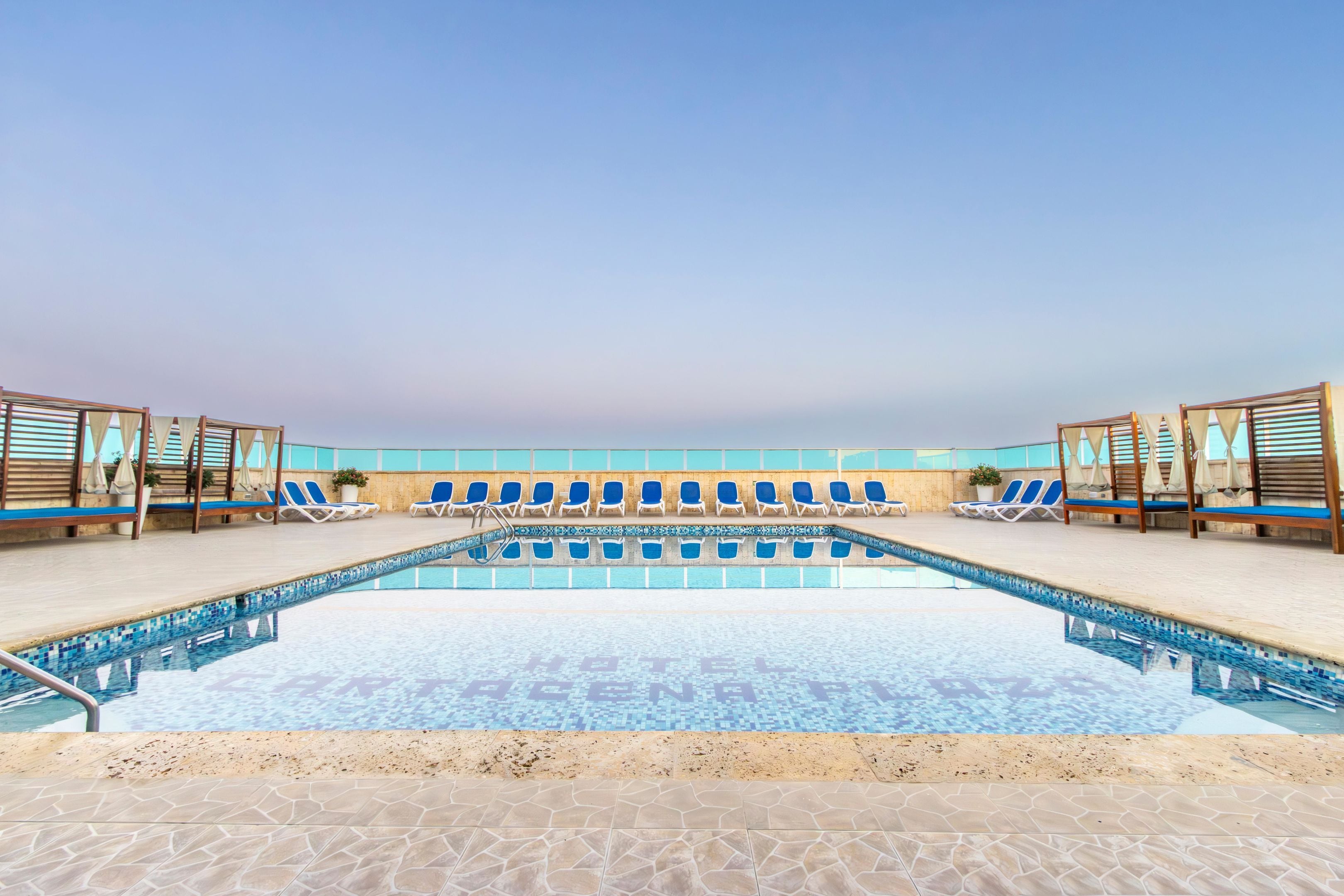 Ein Swimmingpool mit blauen Liegestühlen und Holzsonnenliegen, umgeben von einer gefliesten Terrasse.