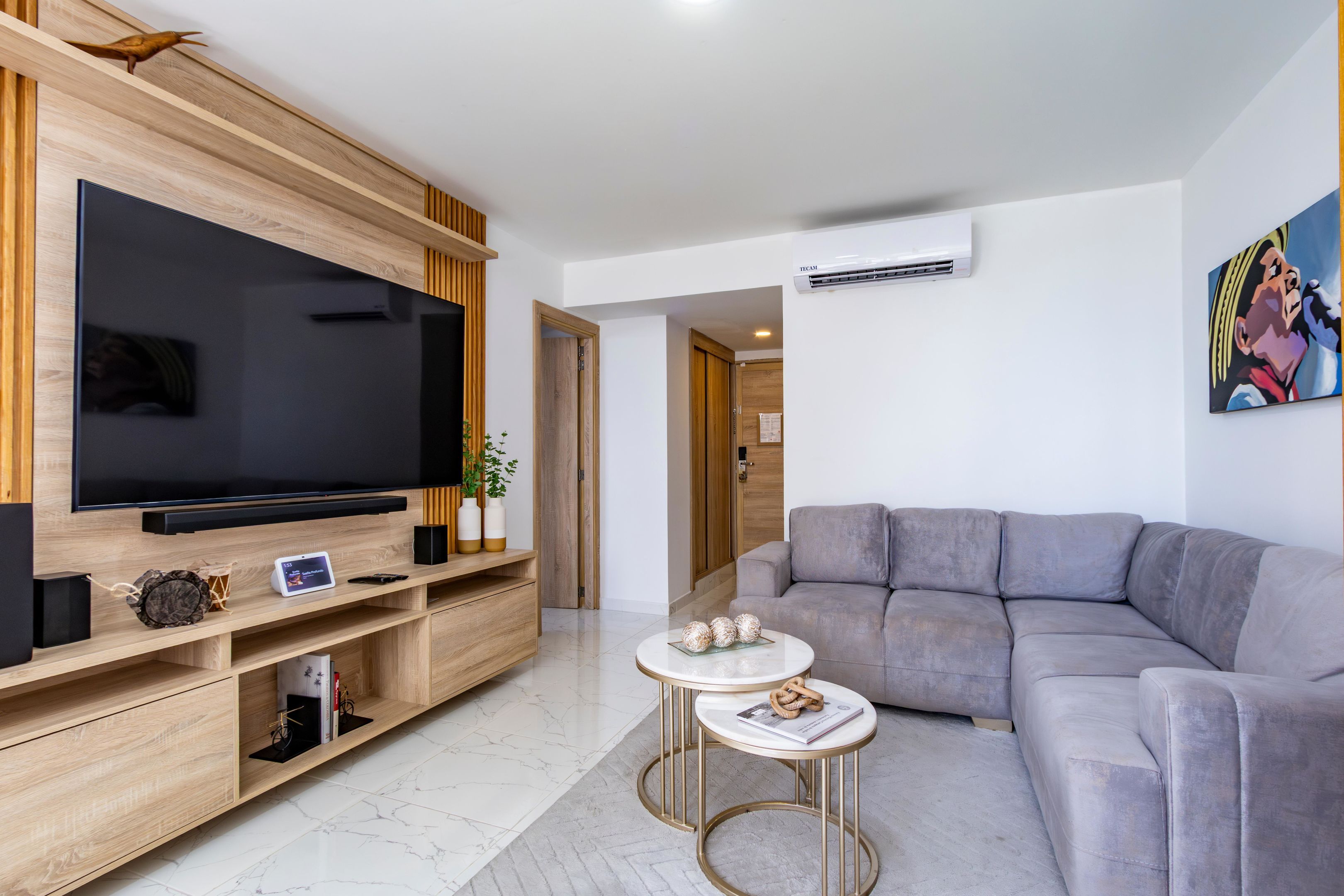 A modern living room with a flat-screen TV, a grey sofa, a small round coffee table, and a wooden entertainment unit.