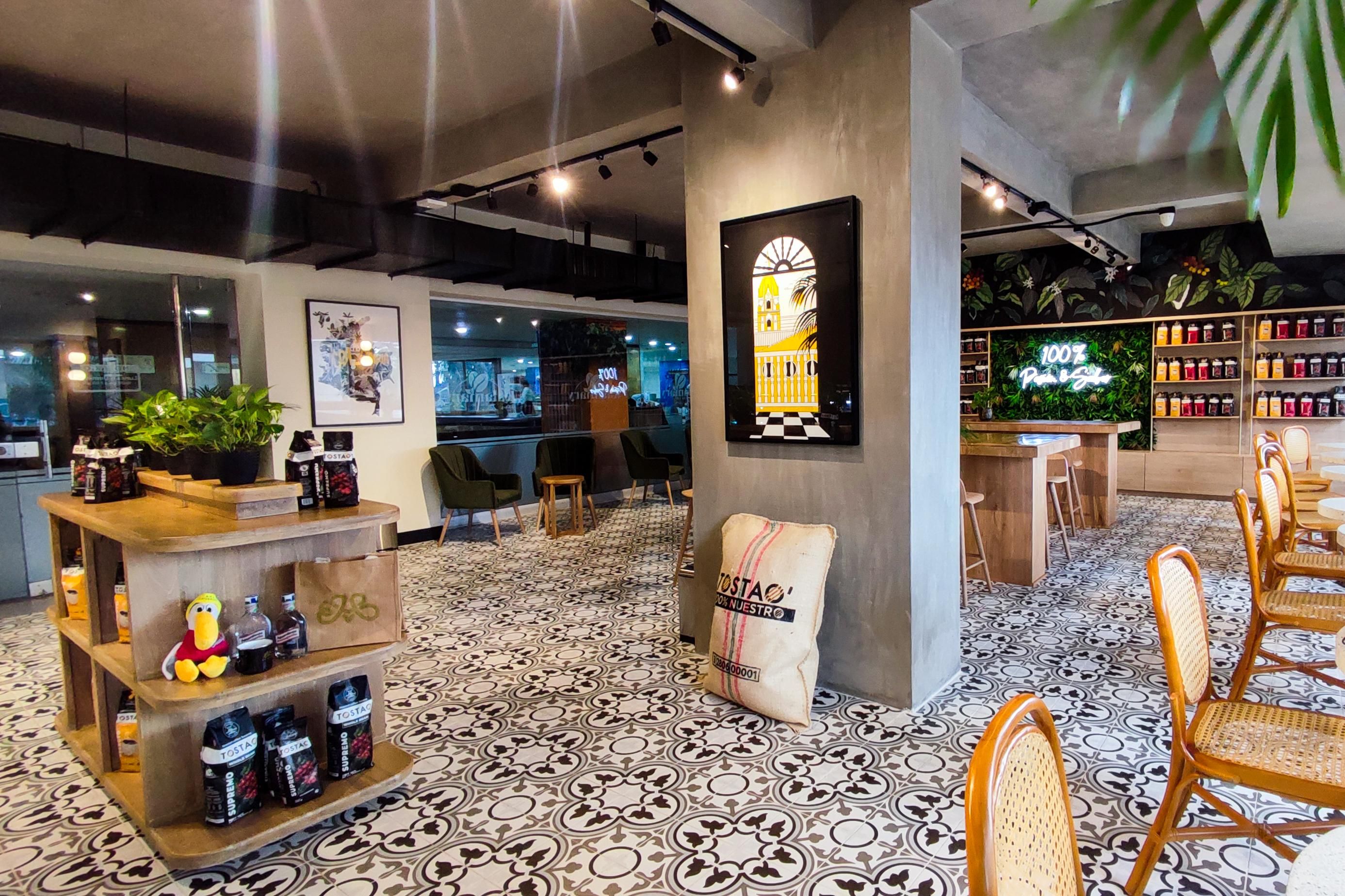 A café interior with a patterned floor, wooden furniture, and a display of Tostac coffee products.