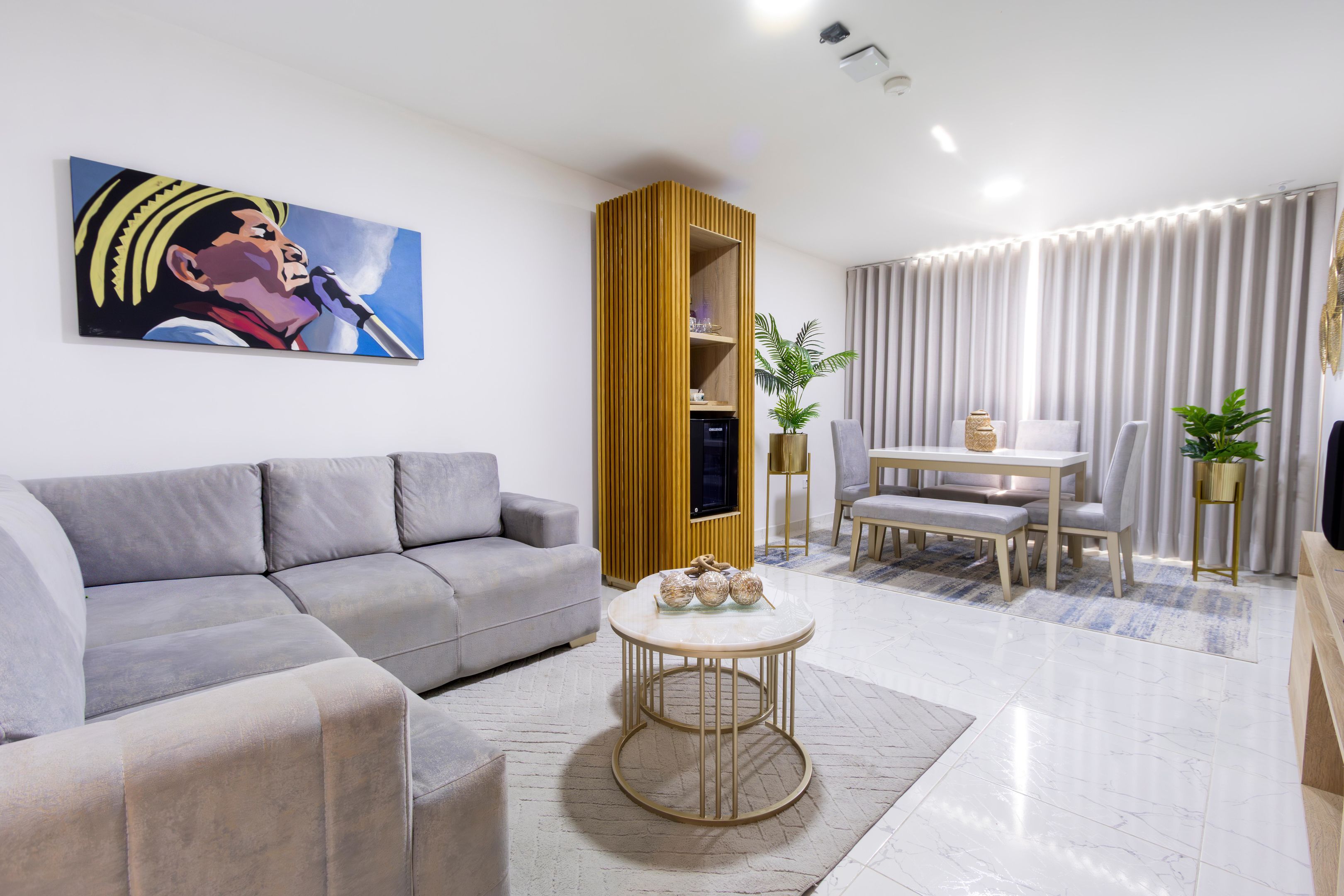 Una sala de estar moderna con un sofá gris, una mesa redonda y un comedor con una mesa y sillas blancas.