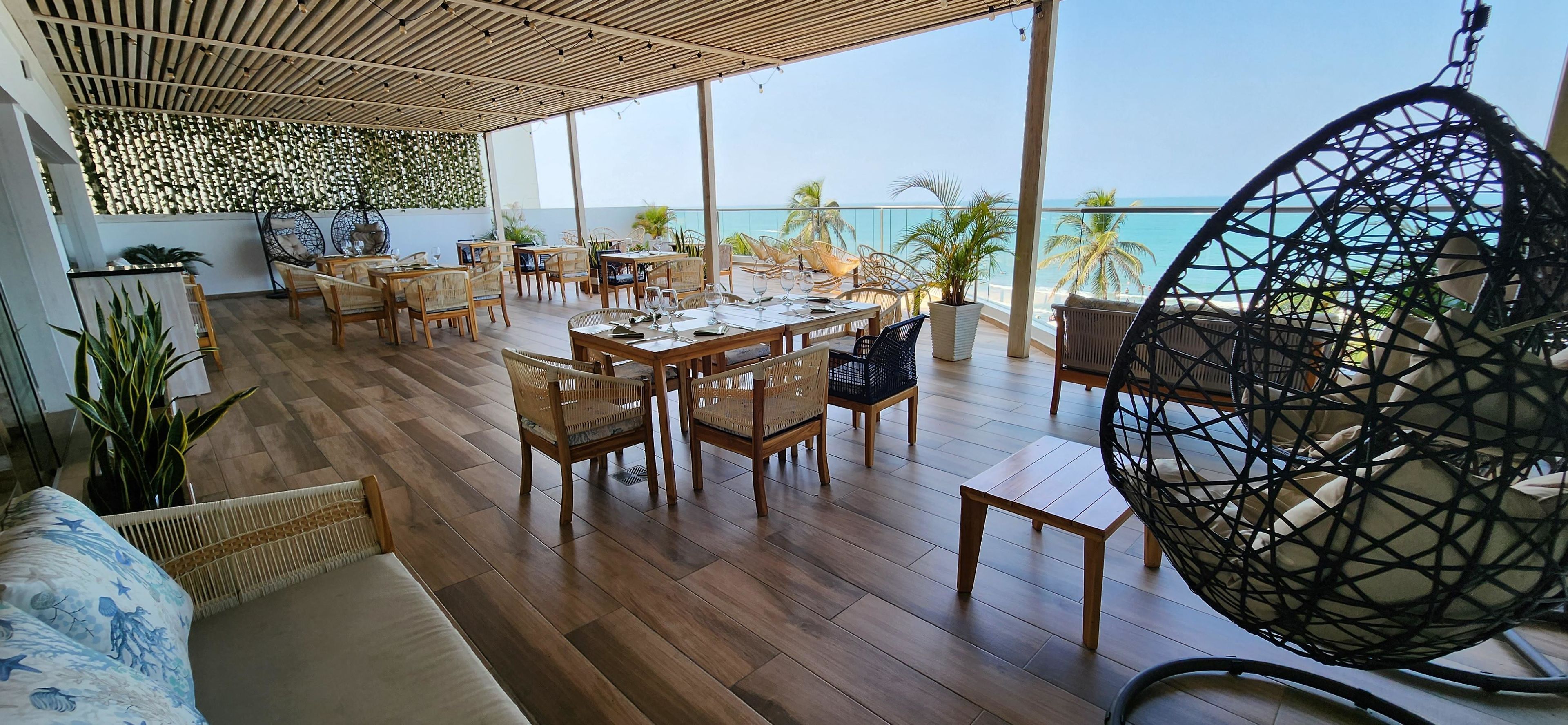 A spacious outdoor area with wooden flooring, multiple seating arrangements including chairs and a hanging chair, and a view of the ocean.