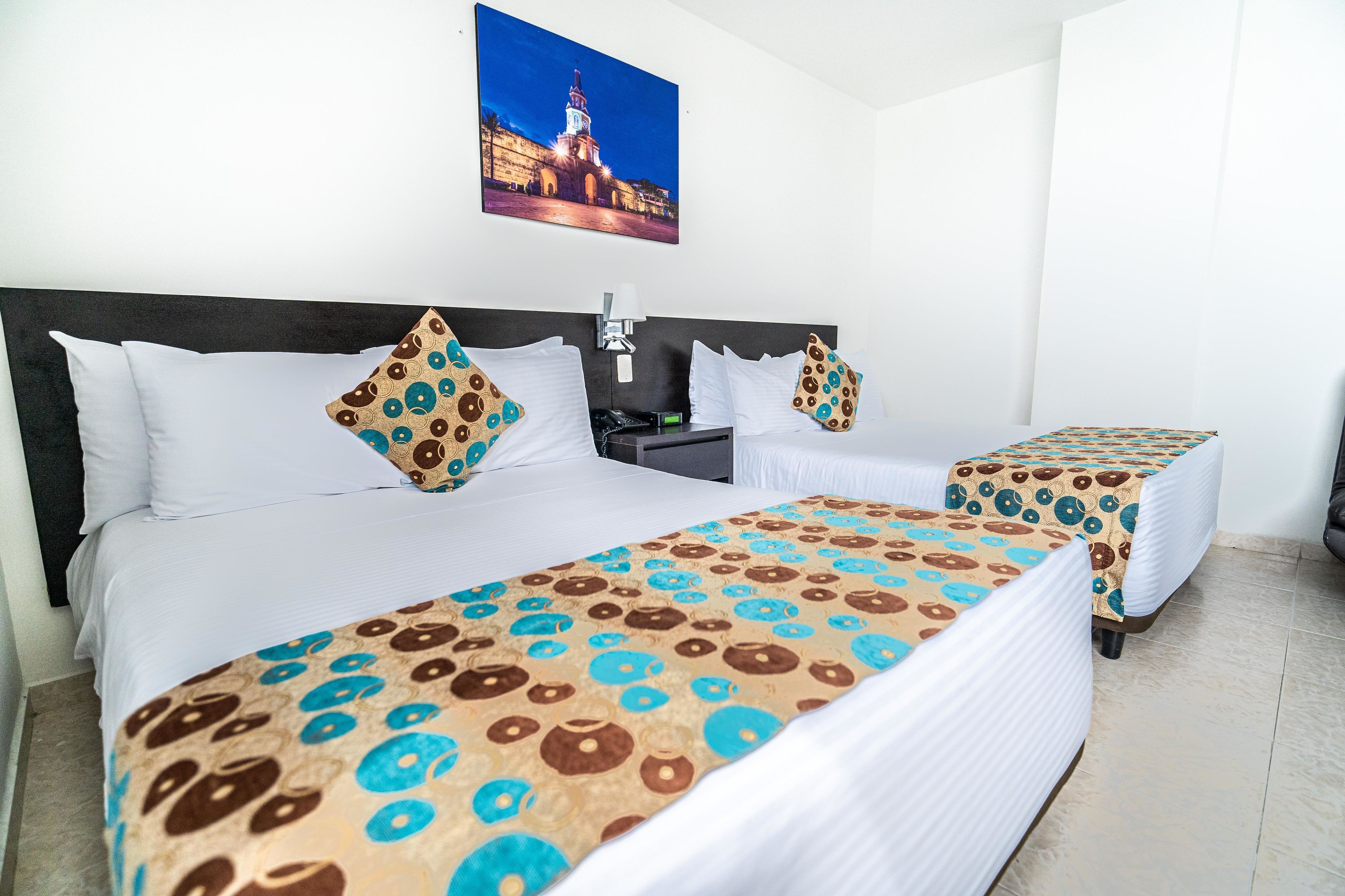A hotel room with two beds, a nightstand, a lamp, and a framed picture on the wall.