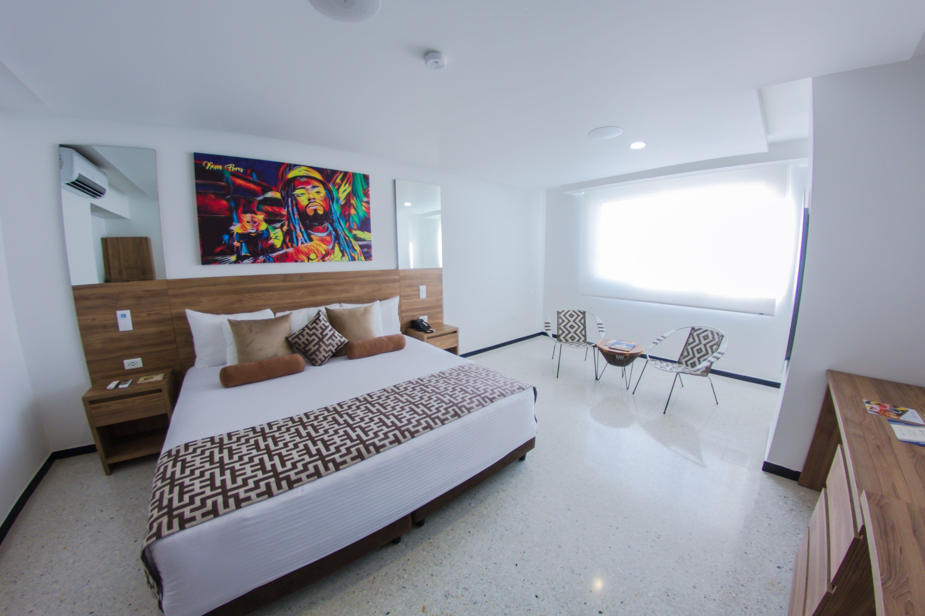 Una habitación de hotel moderna con una cama grande, una mesita de noche, una silla, un escritorio y un ventanal amplio.