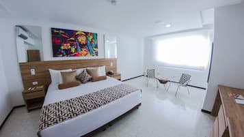 Una habitación de hotel moderna con una cama grande, una mesita de noche, una silla, un escritorio y un ventanal amplio.