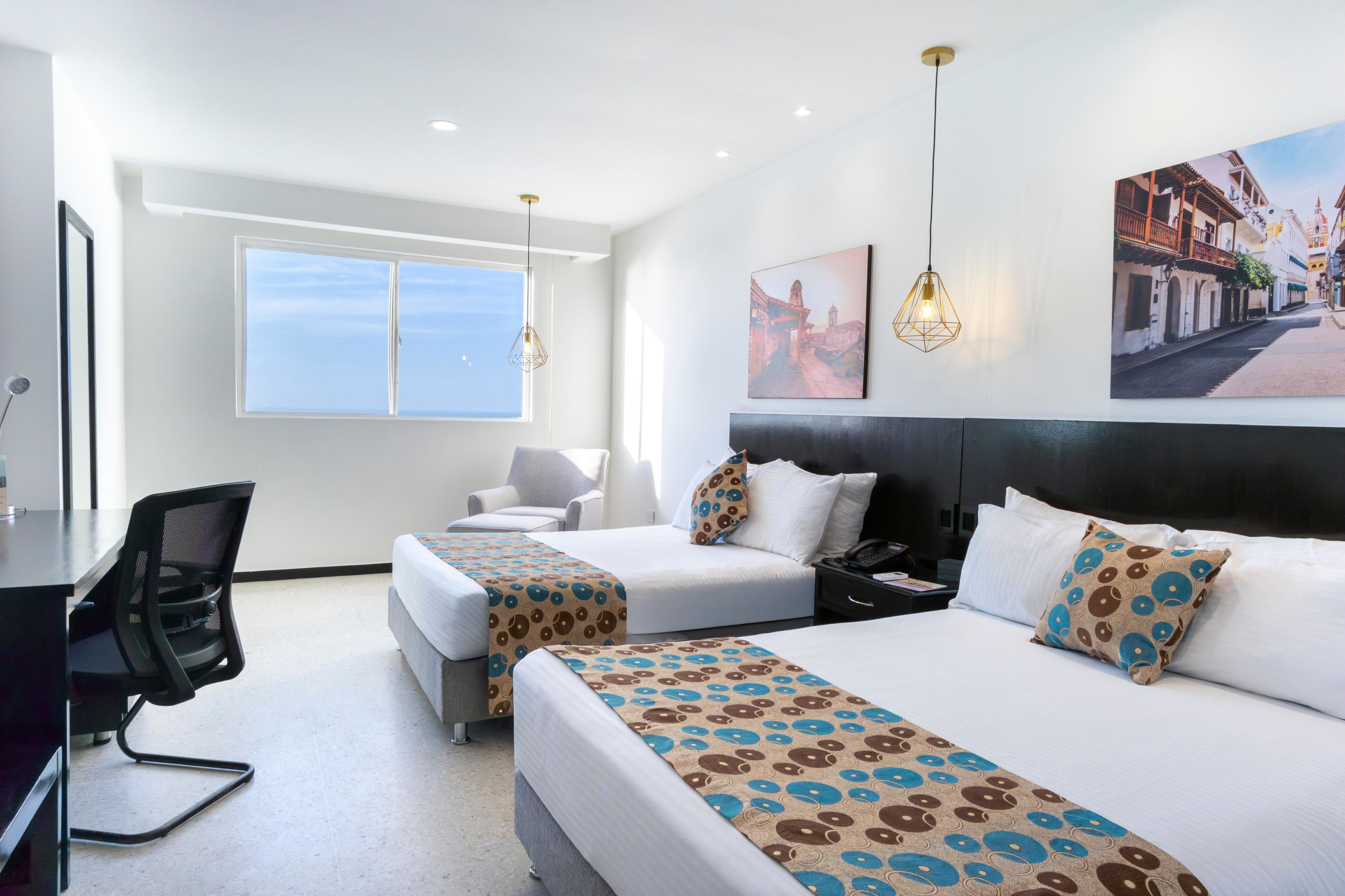 Habitación de hotel con dos camas, un escritorio, una silla, un teléfono y obras de arte en las paredes.