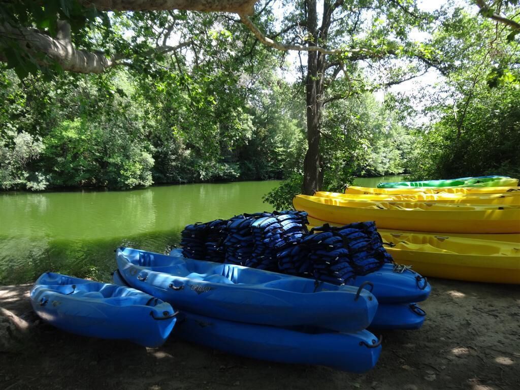 A collection of kayaks and life jackets by a riverbank.
