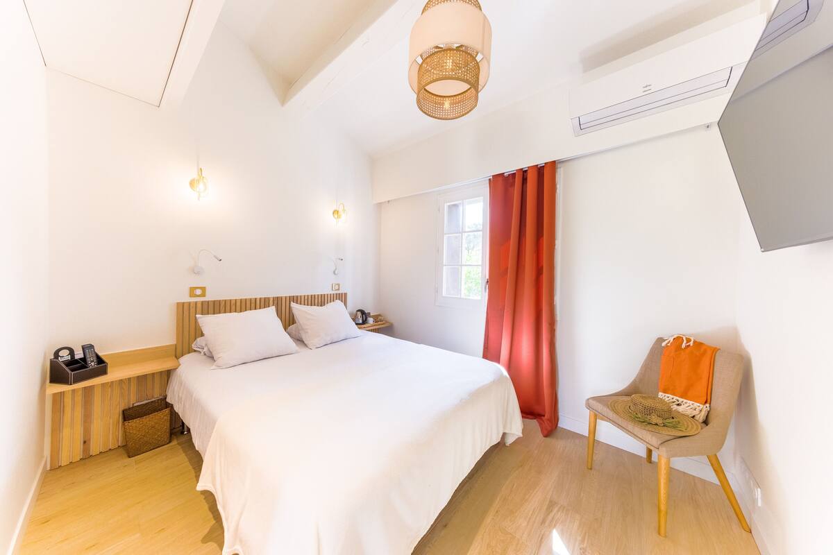 A bedroom with a bed, bedside table, chair, and a window with curtains.