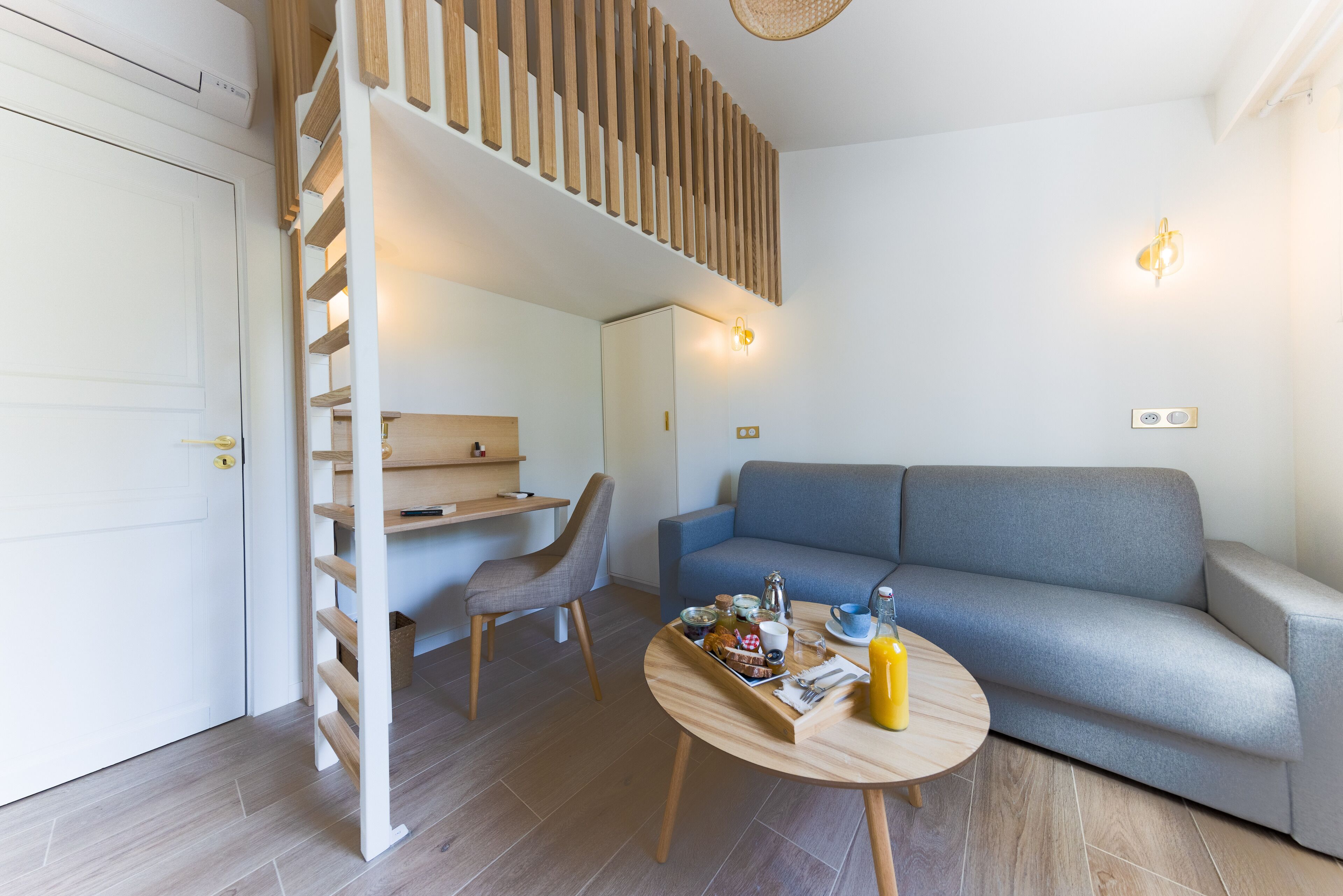 Una sala moderna con un sofá, una mesa de comedor con alimentos para el desayuno, una silla y una escalera que conduce a un nivel superior.