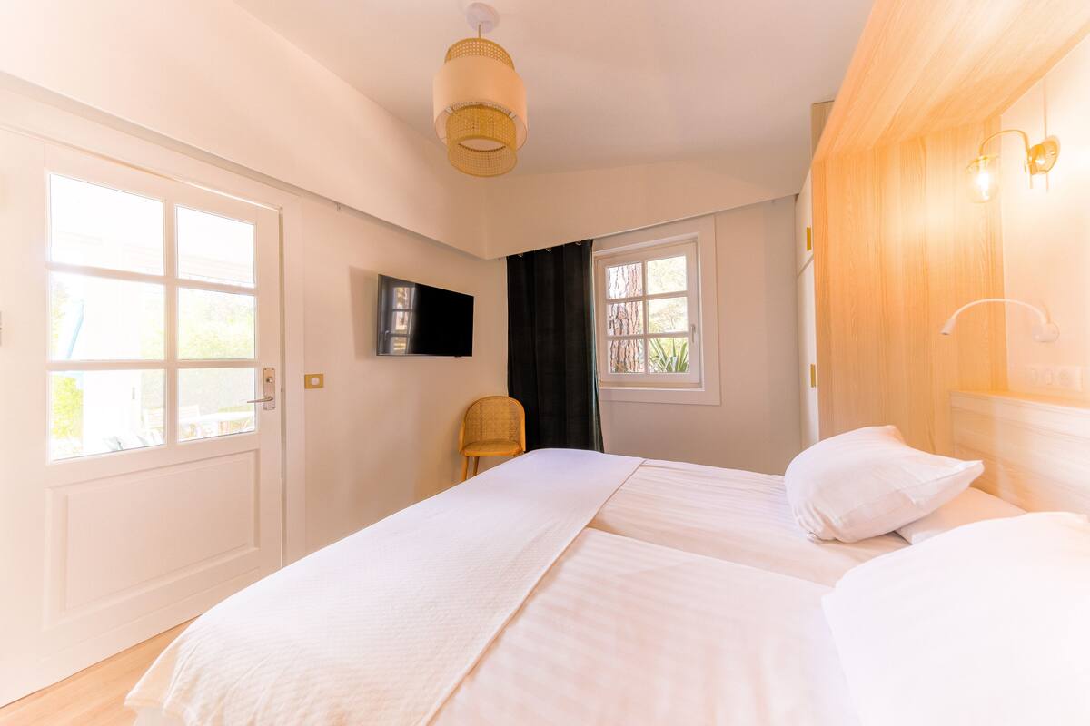A bedroom with two beds, a TV, a chair, and a window.