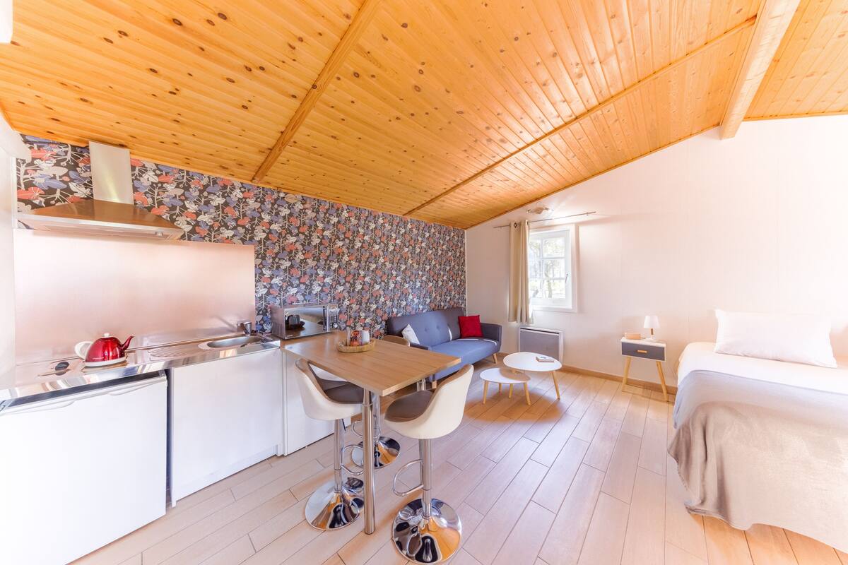A modern kitchen with a wooden ceiling, a dining area with bar stools, a sofa, and a small round table.