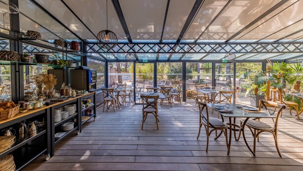A covered outdoor seating area with tables and chairs, surrounded by shelves with various items. - La Villa Vicha, The Originals Relais (Aubais)