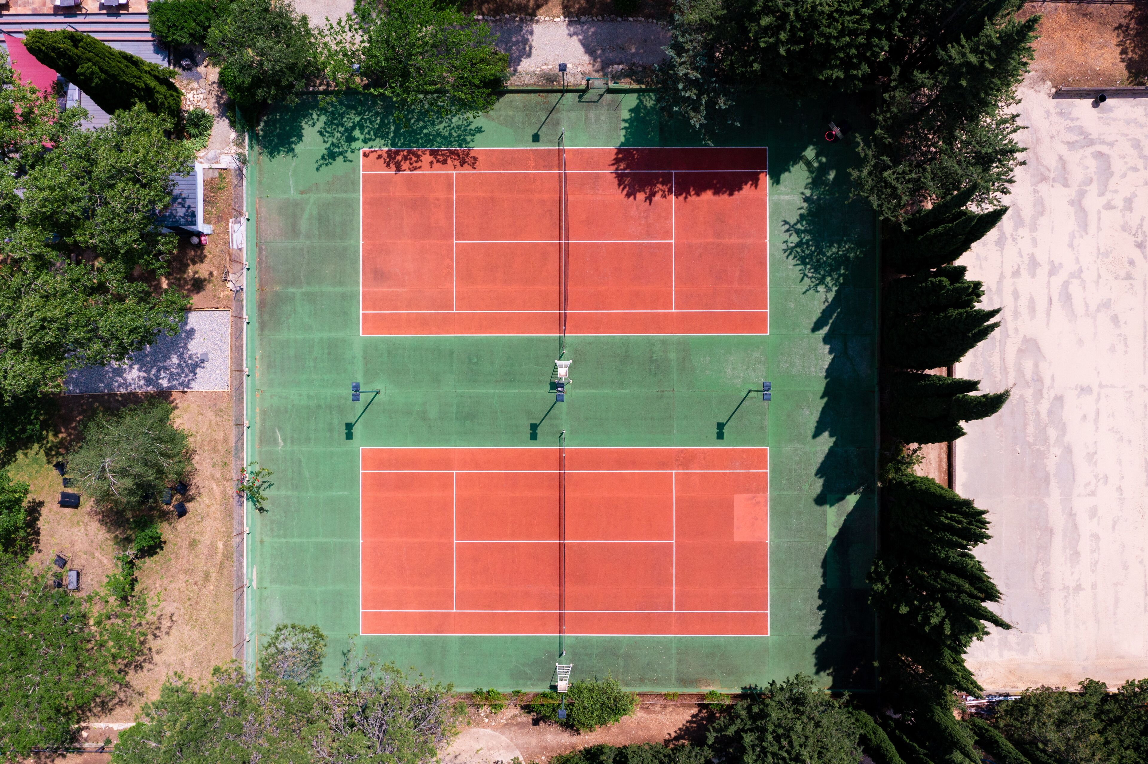 An aerial view of a tennis court with surrounding trees and a building in the background.