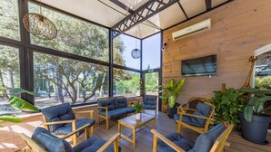 A spacious outdoor seating area with wooden furniture and large windows overlooking a forested area. - La Villa Vicha, The Originals Relais (Aubais)