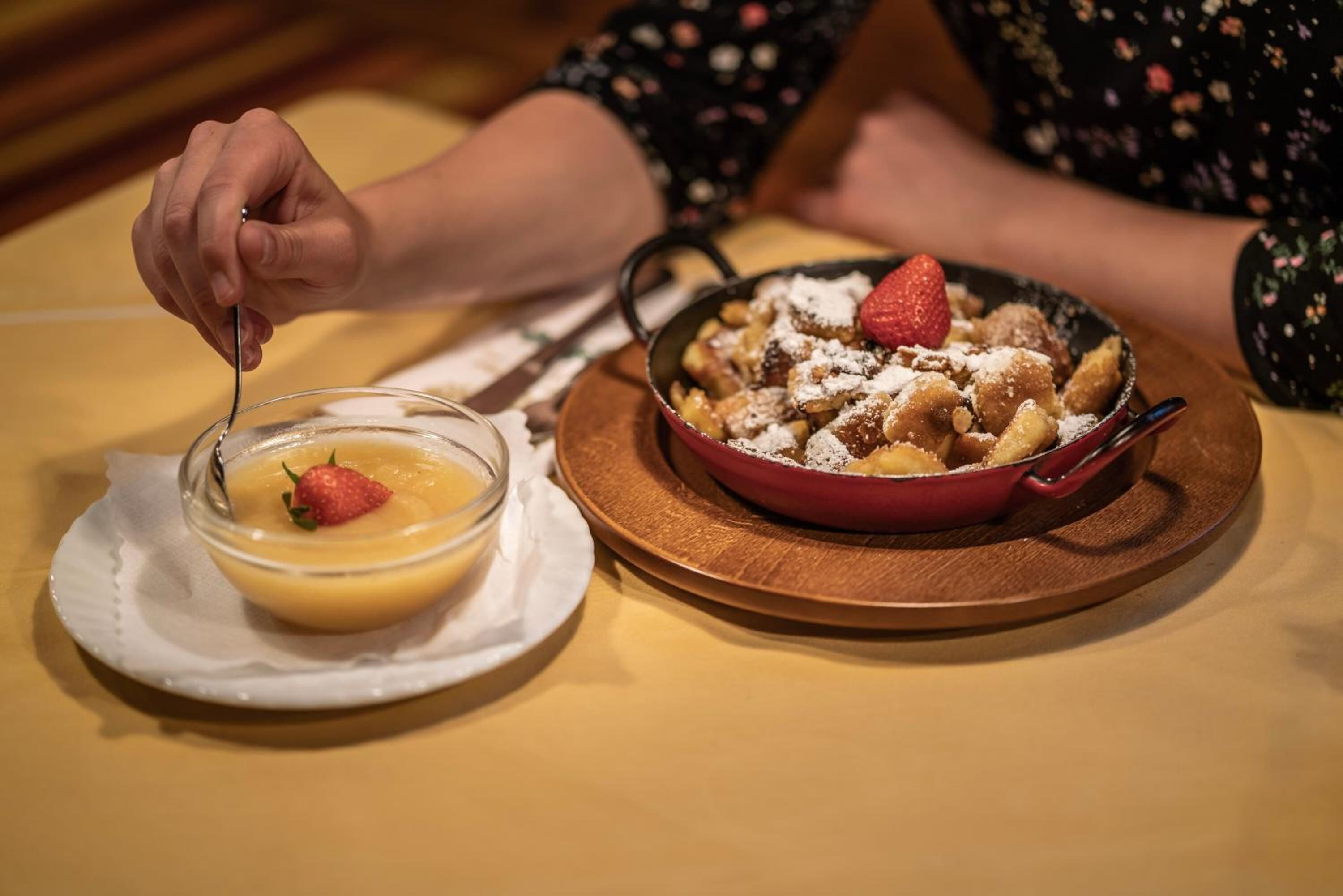 A dessert plate with a bowl of custard and a serving of bread pudding topped with strawberries and powdered sugar.
