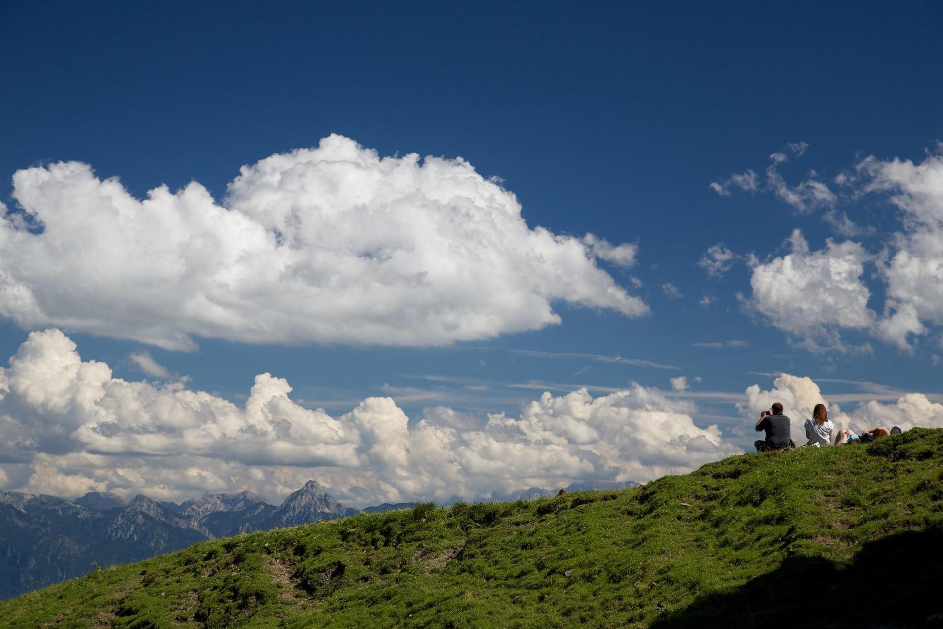 Una colina cubierta de hierba con cielo despejado y montañas al fondo.