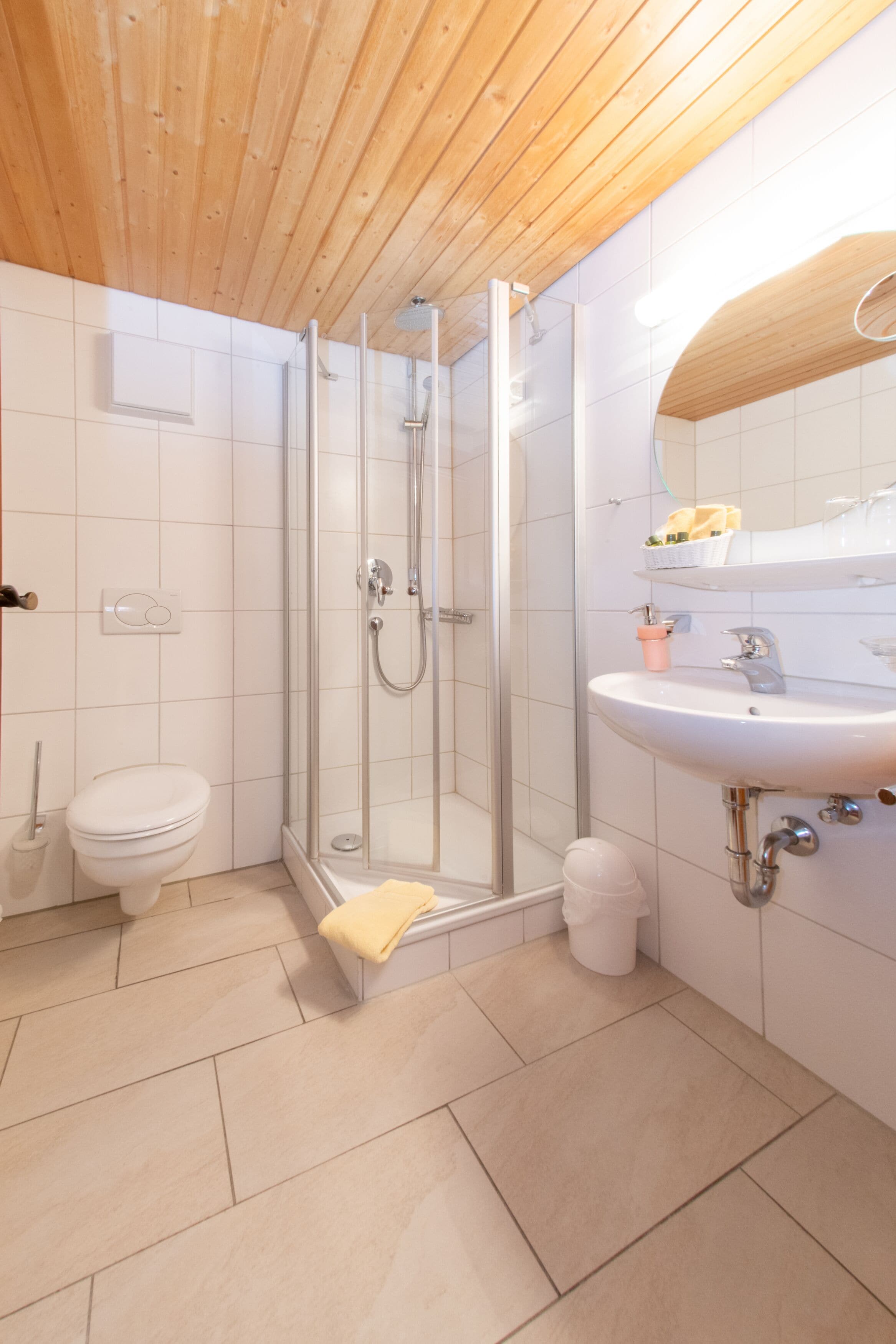 Un baño moderno con ducha de vidrio, inodoro blanco y lavamanos con espejo.