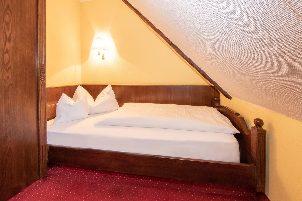 Ein Einzelbett mit Holz Kopfteil, weißer Bettwäsche und einem Teppich mit roten Punkten.