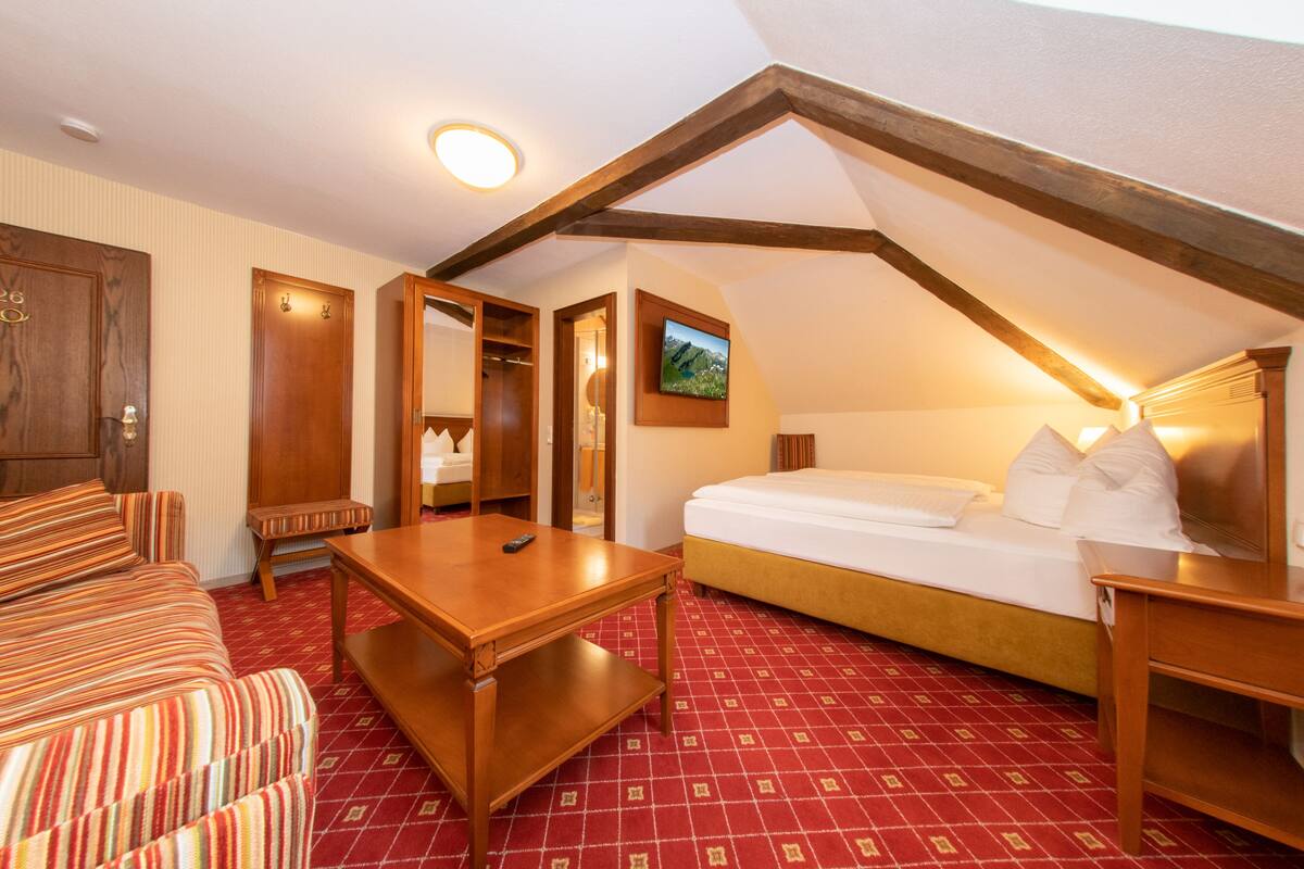 Ein gemütliches Zimmer mit einem Bett, einem Holztisch, einer Bank und einem Fernseher an der Wand.