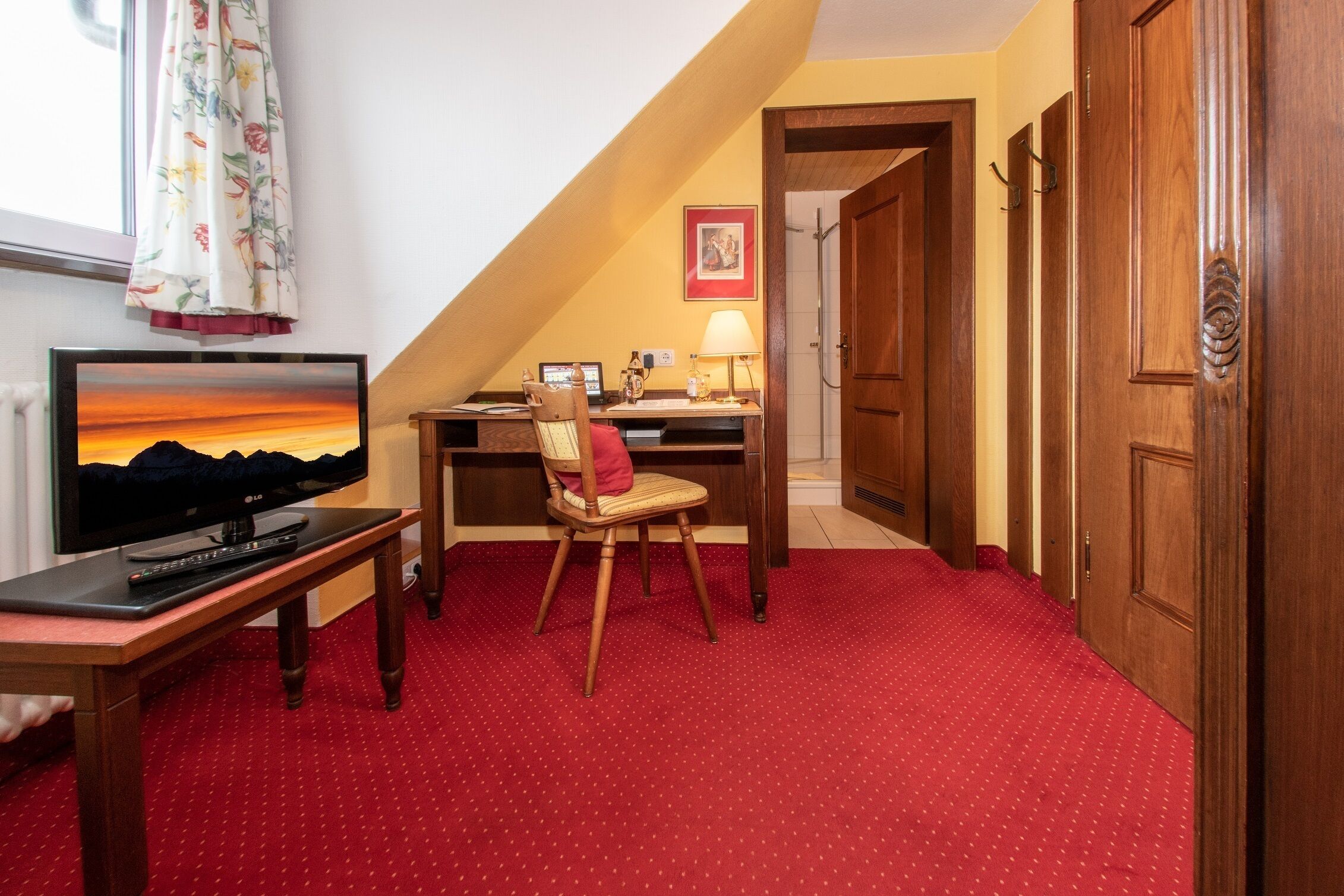 Une pièce équipée d’un téléviseur, d’un bureau, d’une chaise et d’une moquette rouge.