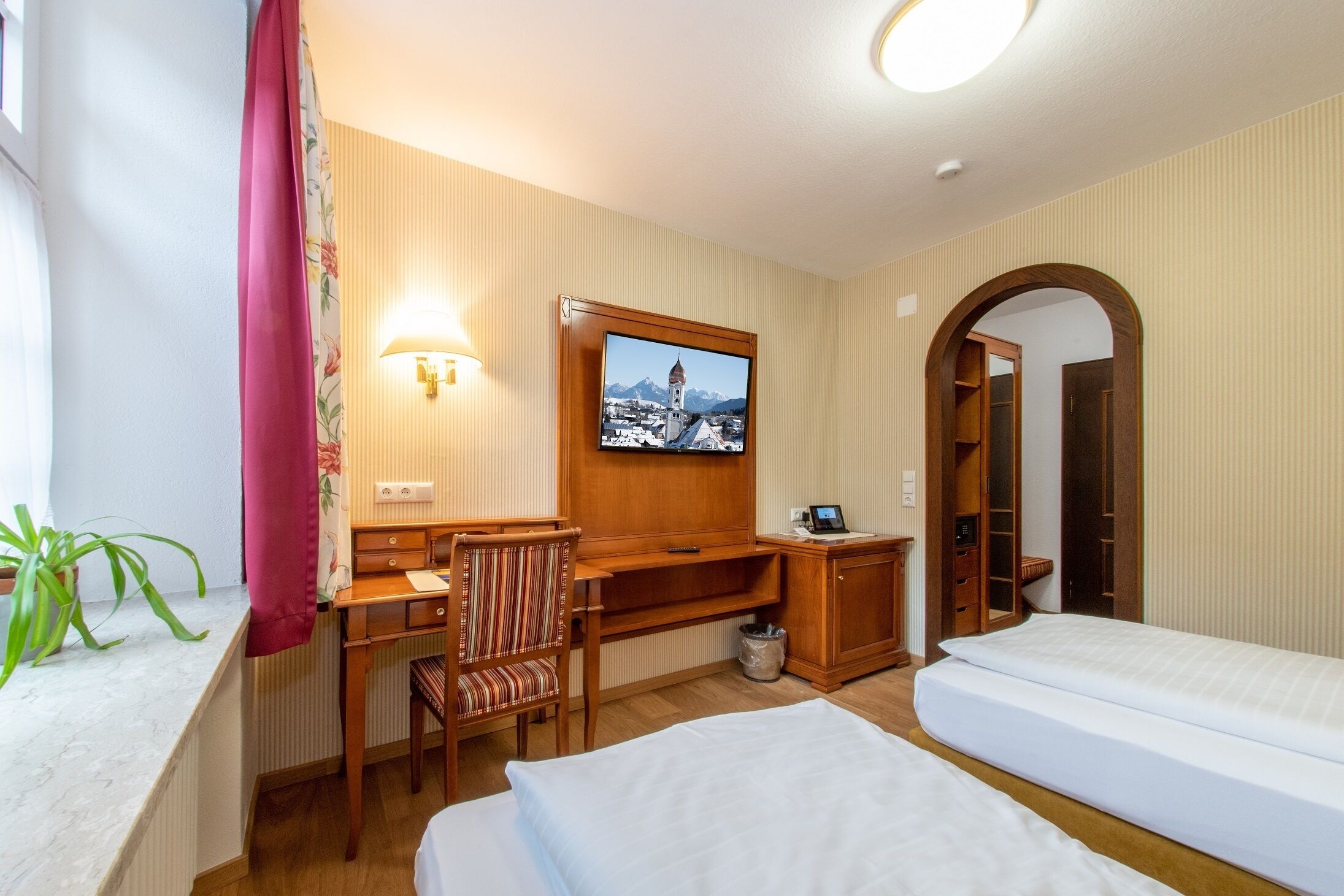 A hotel room with a bed, a desk, a chair, a TV, and a wardrobe.