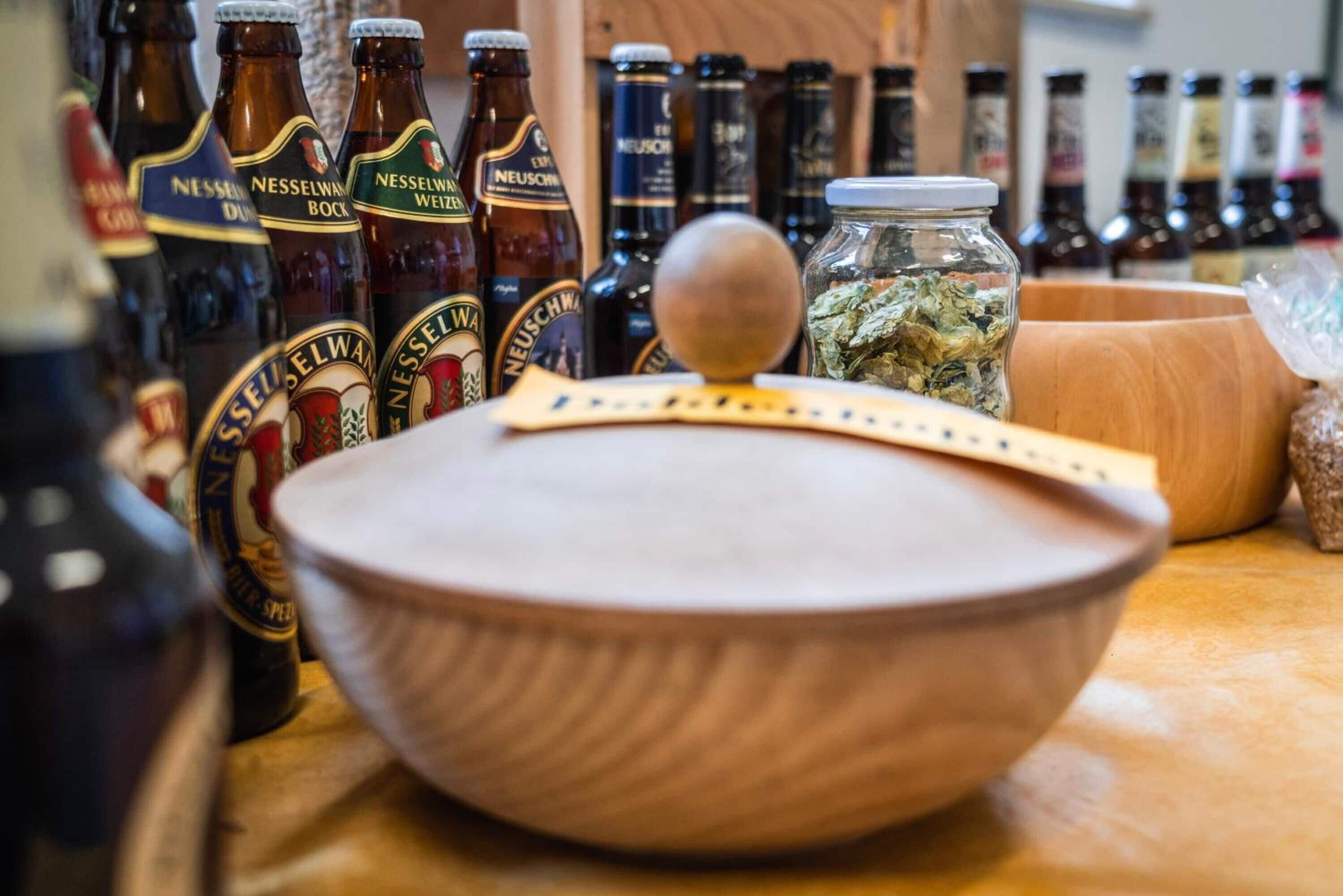 Un cuenco de madera con tapa sobre una mesa, rodeado de botellas de cerveza Nesselman.