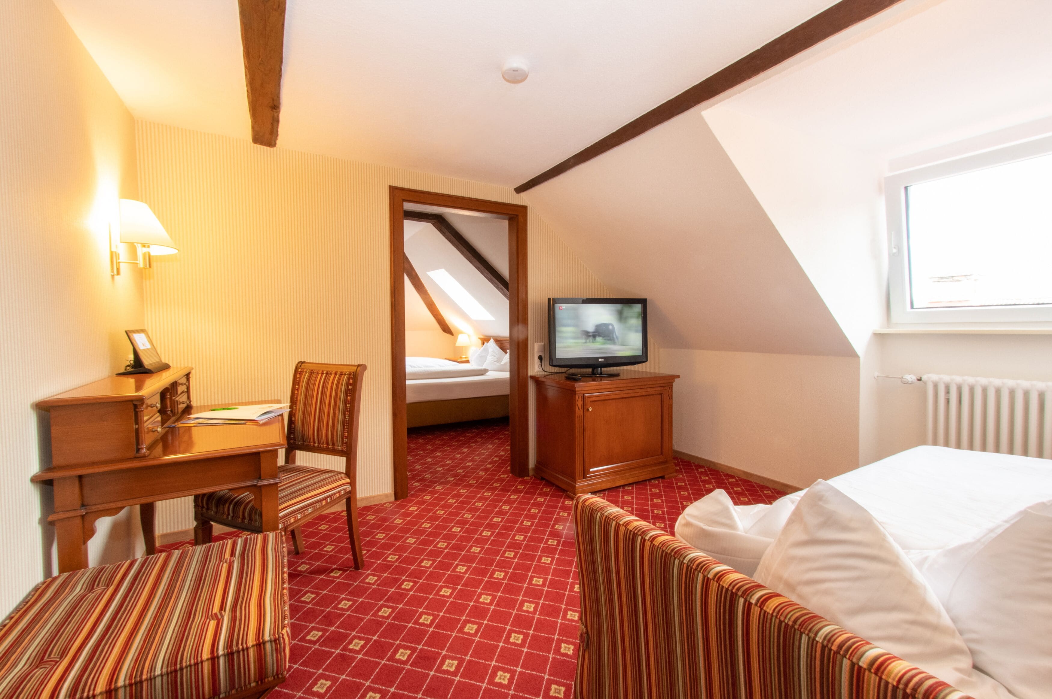 Ein Hotelzimmer mit Bett, Schreibtisch mit Stuhl, Fernseher und Fenster.