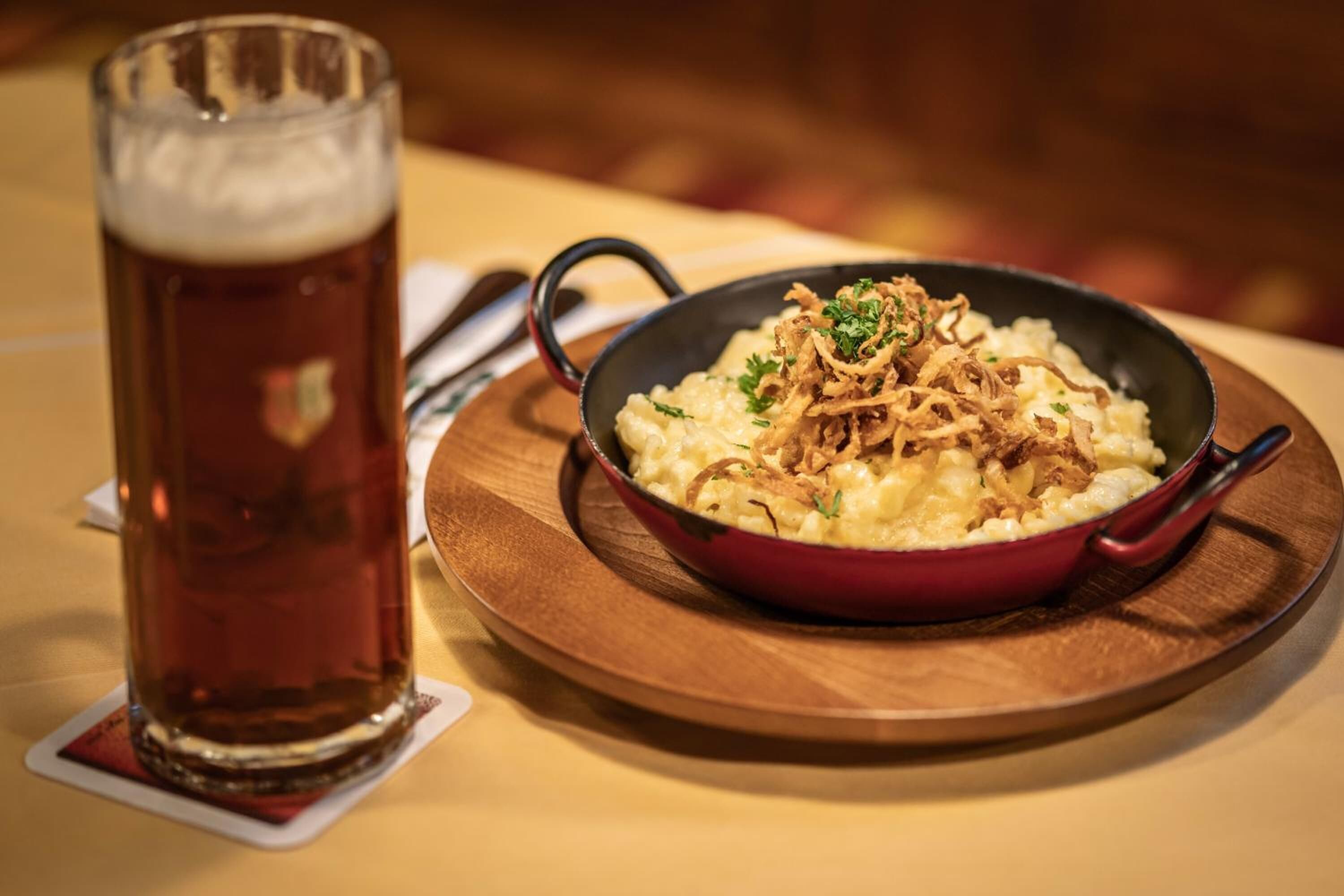 A meal of mashed potatoes with onions and a glass of beer on a wooden table.