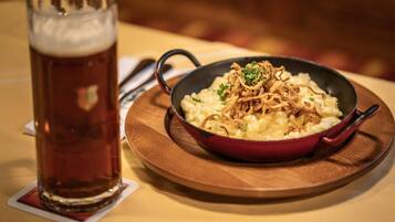 Un plato de puré de patatas con cebolla y un vaso de cerveza sobre una mesa de madera.