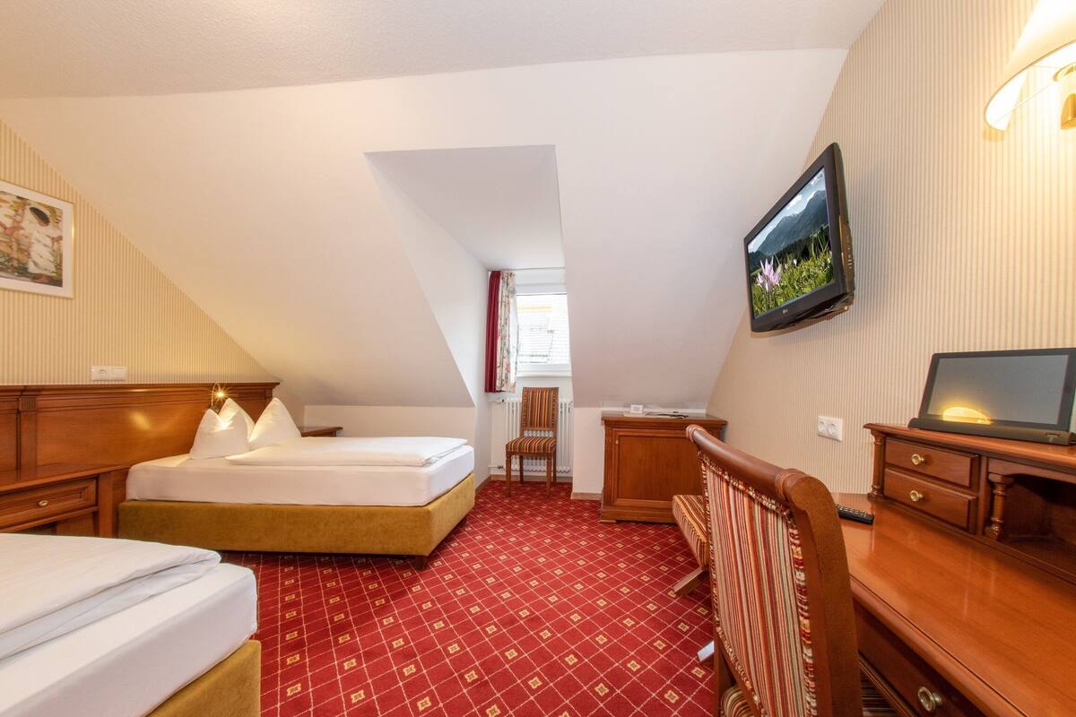 Ein Hotelzimmer mit Bett, Schreibtisch, Stuhl, Fernseher und einem Fenster mit Vorhängen.