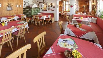A restaurant with wooden walls and tables set with red tablecloths. There are multiple seating areas, including booths and individual tables.