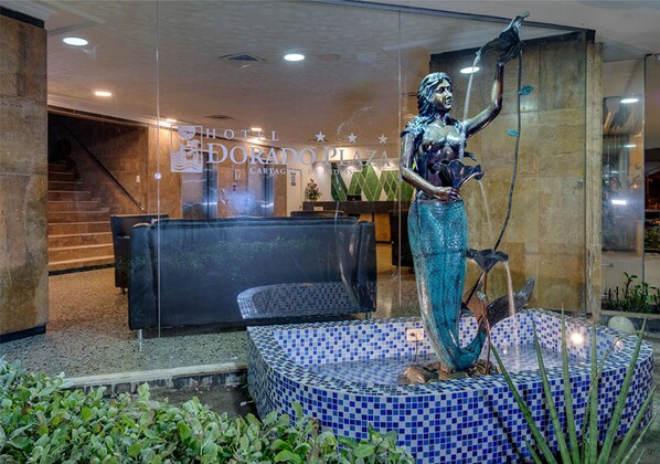 A hotel lobby with a statue of a mermaid, a reception desk, and a staircase.
