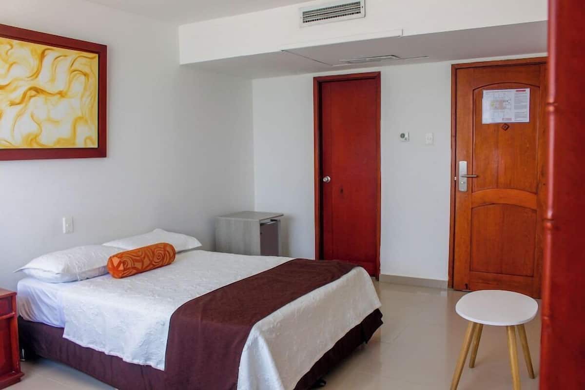Ein Hotelzimmer mit einem Bett, einem kleinen Tisch, einem Mülleimer und einer Tür.
