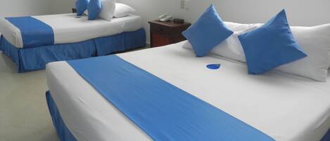 A hotel room with two beds, each with blue and white bedding, a bedside table with a phone, and a window with a view.