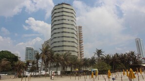 A tall, multi-story hotel with a curved facade, surrounded by palm trees and beach umbrellas. - Hotel Dorado Plaza Bocagrande - All Inclusive (Cartagena)