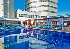 Una piscina con sillas reclinables azules y una zona cubierta con cortinas blancas.