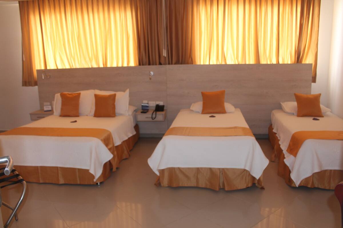 Ein Hotelzimmer mit drei Betten, jedes mit einer weißen und orangefarbenen Bettdecke, und einem hölzernen Kopfteil.