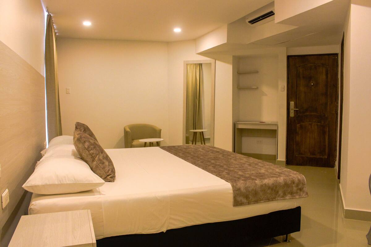 Ein Hotelzimmer mit Bett, Sessel, Schreibtisch und Tür.