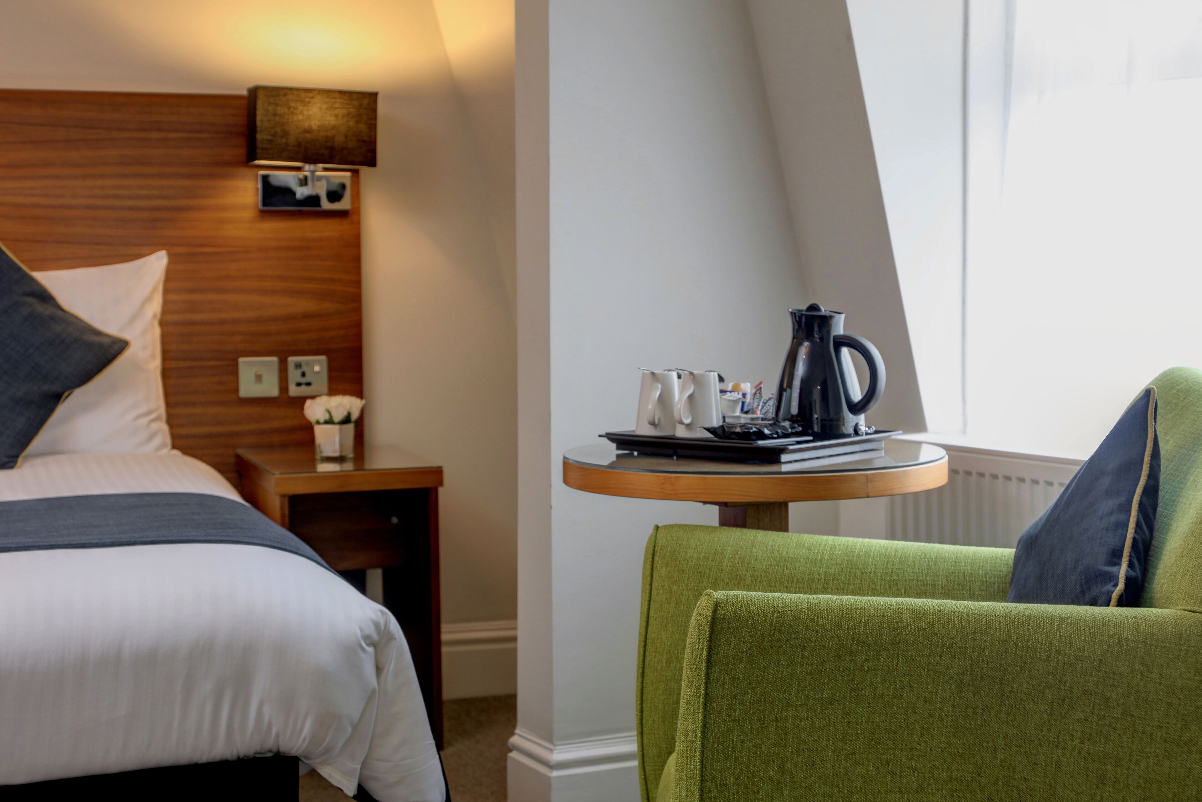 Une chambre d’hôtel avec un lit, une petite table et une bouilloire, ainsi qu’une chaise.