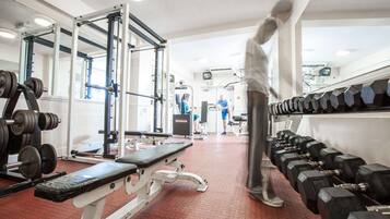Un gimnasio con equipo de levantamiento de pesas, bancos y cintas de correr.