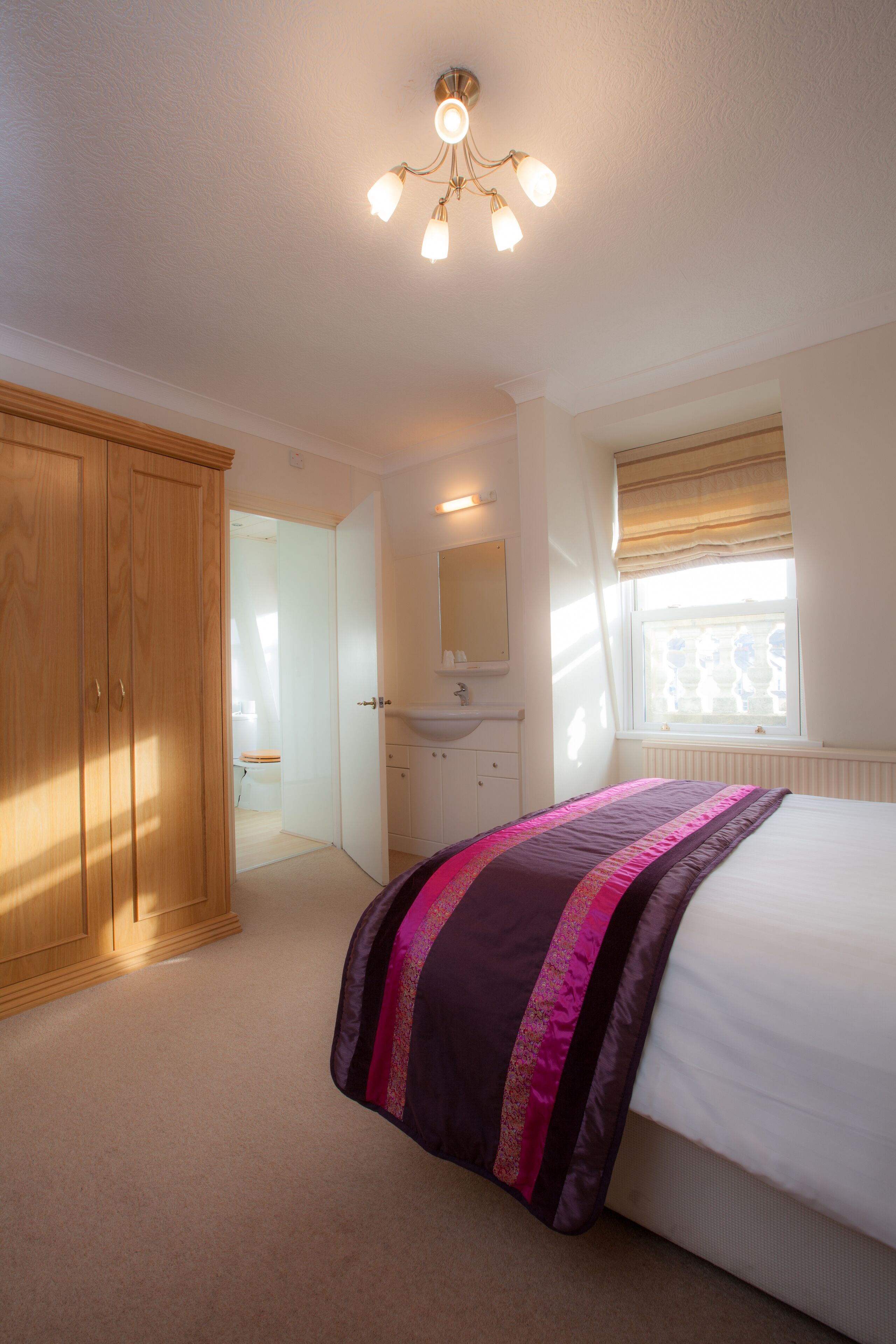 A bedroom with a bed, a wardrobe, a bathroom, and a window with curtains.