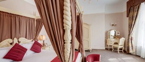 A four-poster bed with curtains, a desk, a chair, and a mirror in a room with a chandelier.